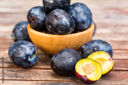 Fresh ripe plums and halves in wooden bowl close