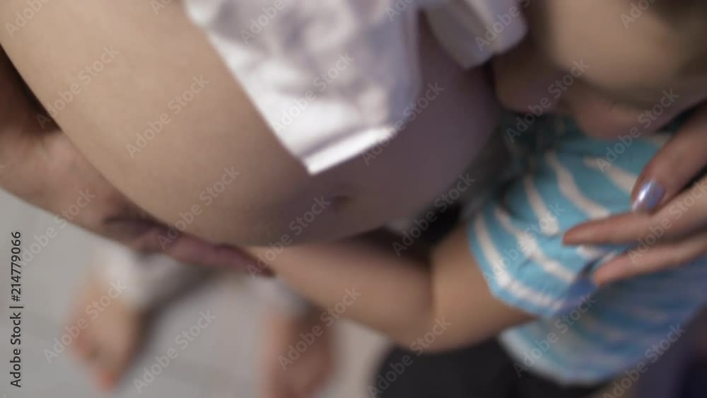 Top view of son hugging pregnant mother and kissing her belly. Child is eager to have junior brother or sister Top view of son hugging pregnant mother and kissing her belly. Child is eager to have junior brother or sister