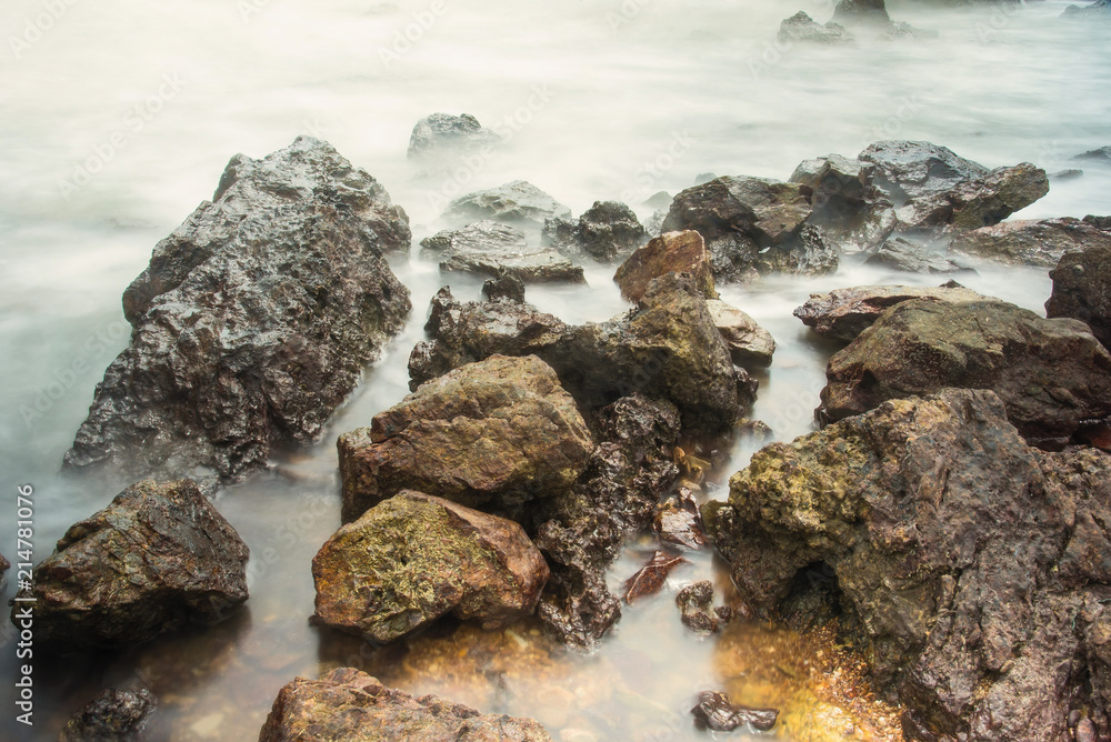 Long exposure seascape with foamy waves splashing against a rocky shore of thailand in the morning time.