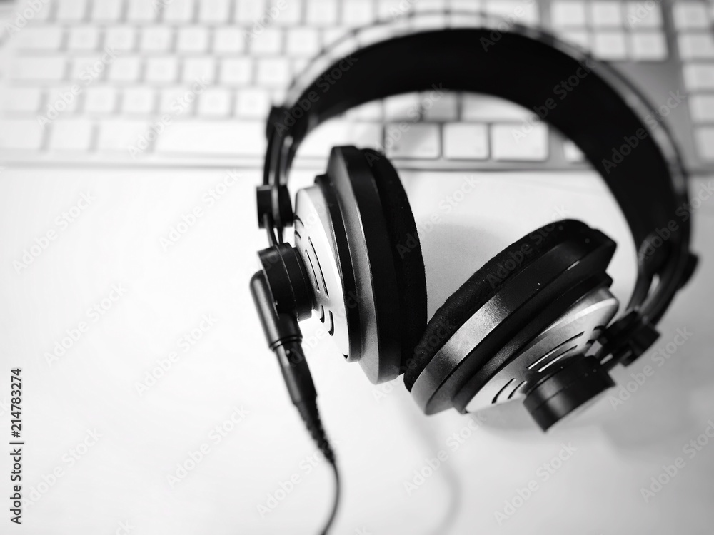 black and white professional headphones with blurred computer keyboard in background. Selective focus. Music and relaxation concept black and white professional headphones with blurred computer keyboard in background. Selective focus. Music and relaxation concept