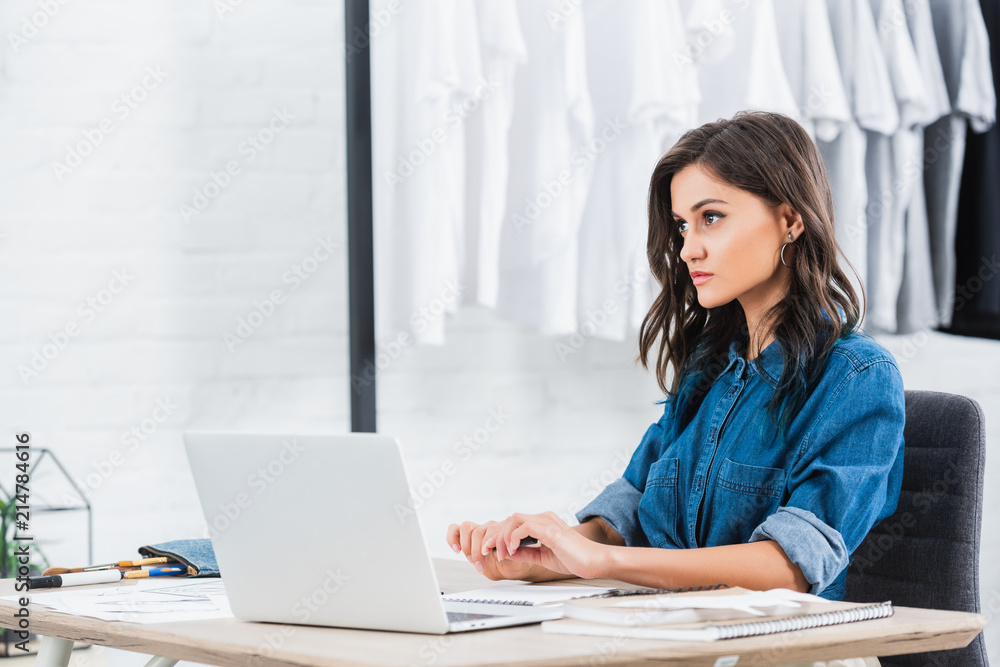 attractive female fashion designer working at table with laptop attractive female fashion designer working at table with laptop