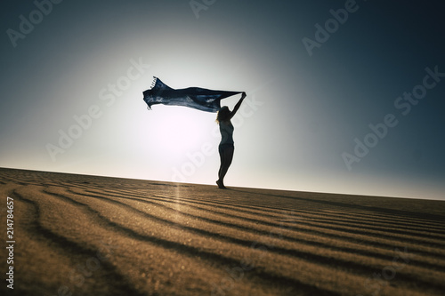 beautiful thin body woman enjoy freedom and summer travel laying with the wind in the desert sand. beach and vacation concept for freedom and joyful leisure activity. outdoor desert and silhouette 