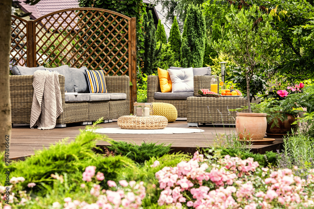 Wooden terrace with couch with pillows, armchair, table with fresh fruits and candles on wicker footrest Wooden terrace with couch with pillows, armchair, table with fresh fruits and candles on wicker footrest