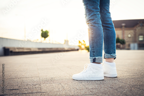 High tops. Girl in blue jeans and white sport shoes standing on the ground