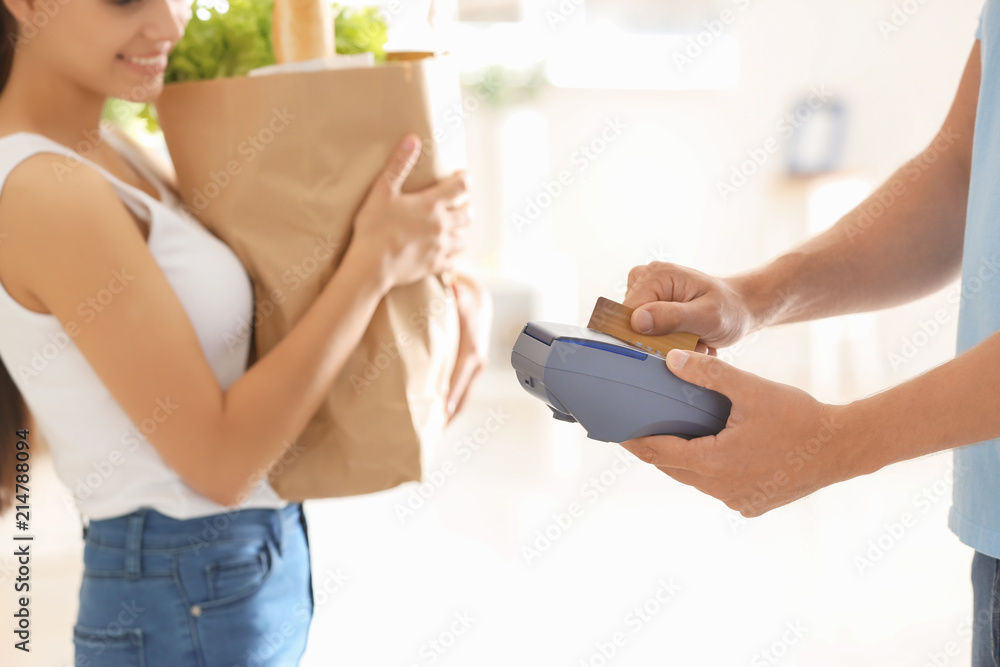 Young woman using bank terminal to pay for food delivery indoors Young woman using bank terminal to pay for food delivery indoors