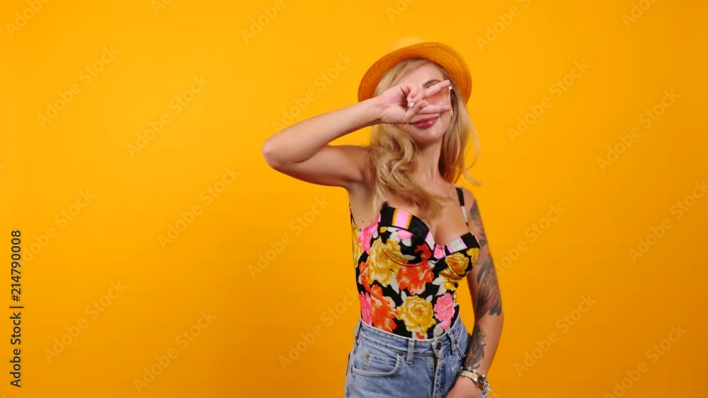 Happy sexy woman wearing sunglasses and a hat dances and smiles to the camera isolated on yellow orange background. Happines, travel, vacation and summer concept footage Happy sexy woman wearing sunglasses and a hat dances and smiles to the camera isolated on yellow orange background. Happines, travel, vacation and summer concept footage