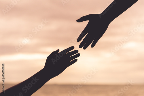 silhouette helping hands on blurred sea and sky background. Friendship Day concept.
