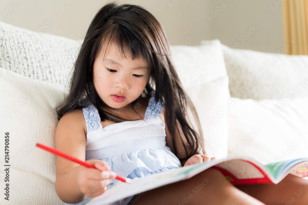 Happy cute little girl smiling and holding red pencil and drawing, writing on a book to do homework. kid education concept.