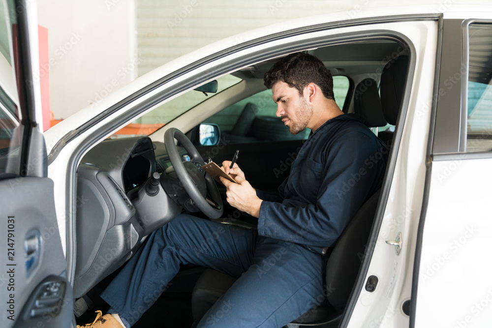 Male Technician Preparing Checklist In Car At Repair Shop