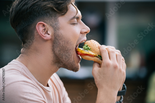 Murais de parede side view of man eating tasty burger with closed eyes