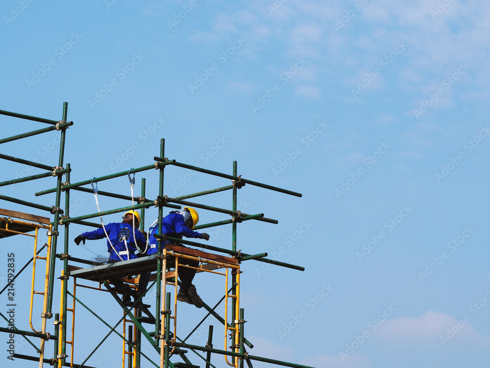 Construction workers working on scaffolding with blue sky at construction site Construction workers working on scaffolding with blue sky at construction site