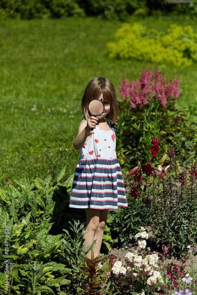 Little girl 4-5 years old with a magnifying glass in her hand. The child walks around the garden and studies plants and flowers. Little girl 4-5 years old with a magnifying glass in her hand. The child walks around the garden and studies plants and flowers.