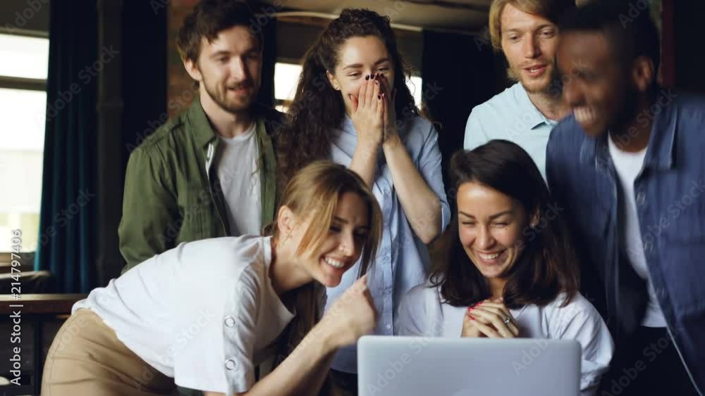 Pretty brunette is working with computer and laughing, her team is coming to congratulate her on good results, people are clapping hands and talking. Pretty brunette is working with computer and laughing, her team is coming to congratulate her on good results, people are clapping hands and talking.