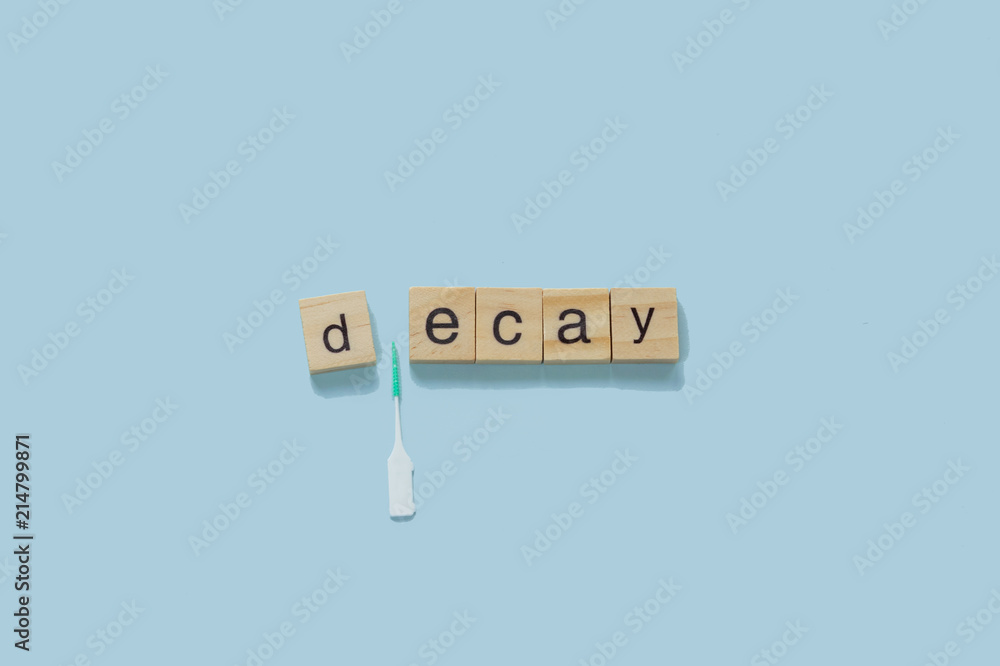 Dental hygiene concept: word decay spelled with wooden tiles on a blue background - interdental brush between the letters Dental hygiene concept: word decay spelled with wooden tiles on a blue background - interdental brush between the letters