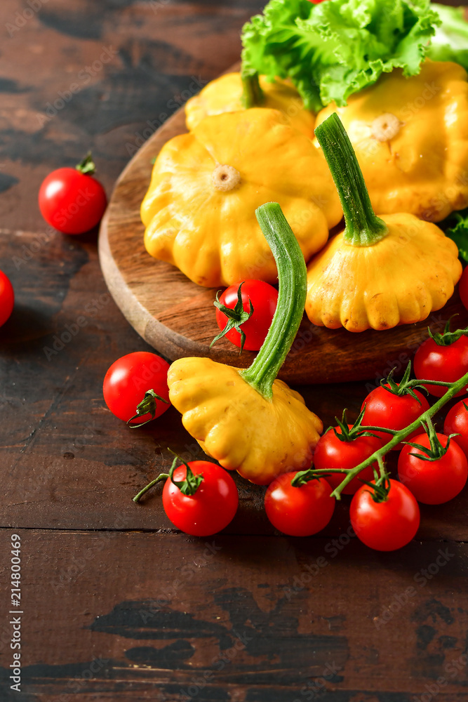 organic yellow patissons with cherry tomatoes and salad on a wooden table. a new harvest of vegetables from the garden, vegan food, a diet food. selective focus and copy space organic yellow patissons with cherry tomatoes and salad on a wooden table. a new harvest of vegetables from the garden, vegan food, a diet food. selective focus and copy space