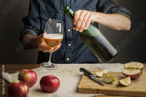 Fotografia Male hands pouring premium cidre in wine glass above rustic wood table