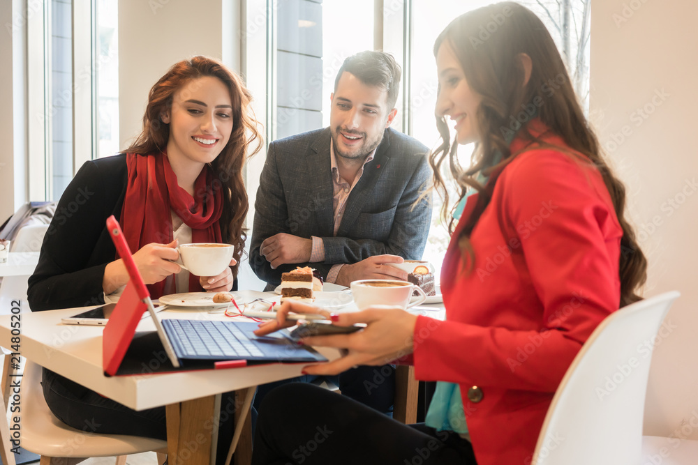 Three young colleagues wearing smart casual outfits while relaxing during coffee break in a trendy cafeteria with wireless connection to the internet Three young colleagues wearing smart casual outfits while relaxing during coffee break in a trendy cafeteria with wireless connection to the internet