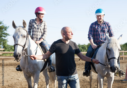 Positive mature couple with jockey learn to riding horse at farm