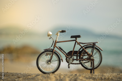 Fototapeta Naklejka Na Ścianę i Meble -  bicycle transport toy on sand sea beach in the evening sunset sky , with yellow light beam