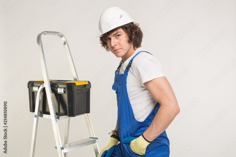 Construction, building and workers concept - Curly haired builder with toolbox and white helmet in studio. Construction, building and workers concept - Curly haired builder with toolbox and white helmet in studio.