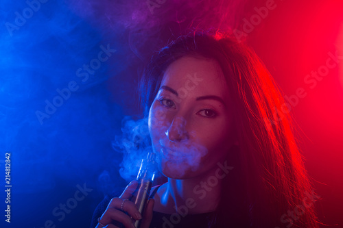 Portrait of girl in colored neon smoke with vape or electronic cigarette.