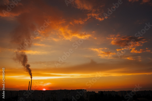 Colorful Magic Sunset. Roofs of city houses during sunrise. Birds flying in the sky. Dark smoke coming from the thermal power plant pipe.