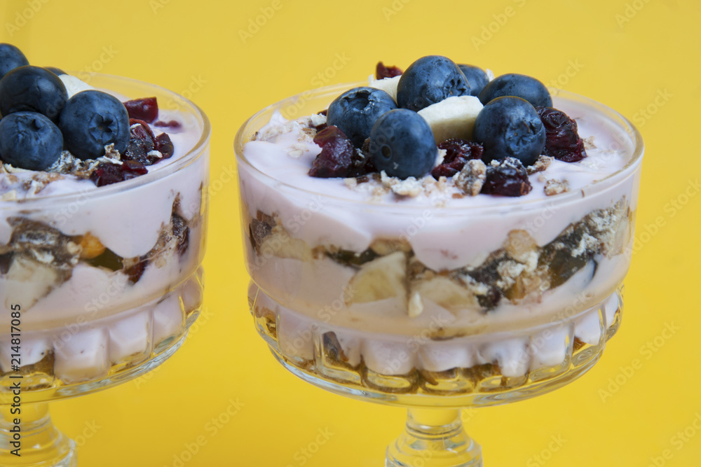 Breakfast in glass cup. Close up granola oat meals,with dried fruits, blueberries and yogurt. Isolated on yellow background. Breakfast in glass cup. Close up granola oat meals,with dried fruits, blueberries and yogurt. Isolated on yellow background.