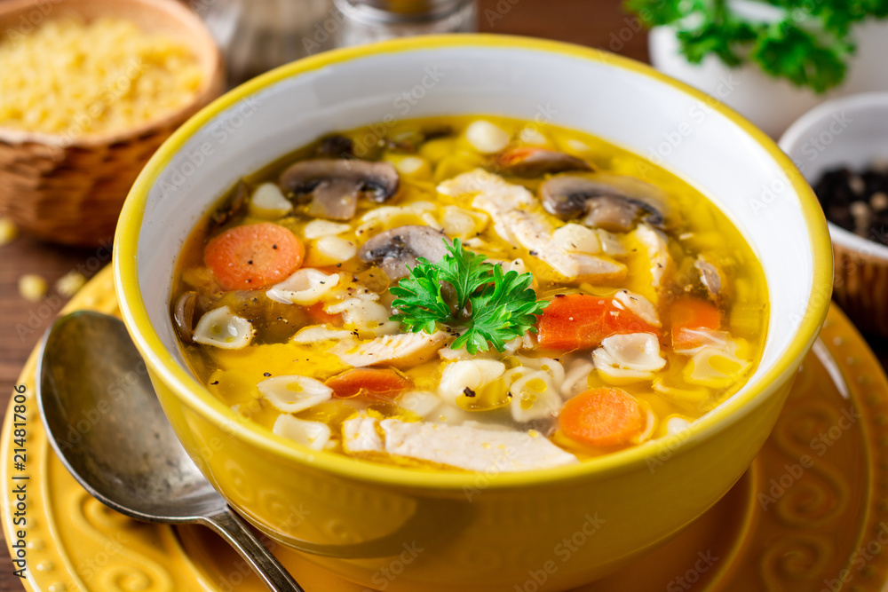 Chicken soup with mushrooms, vegetables and pasta in bowl on wooden table.