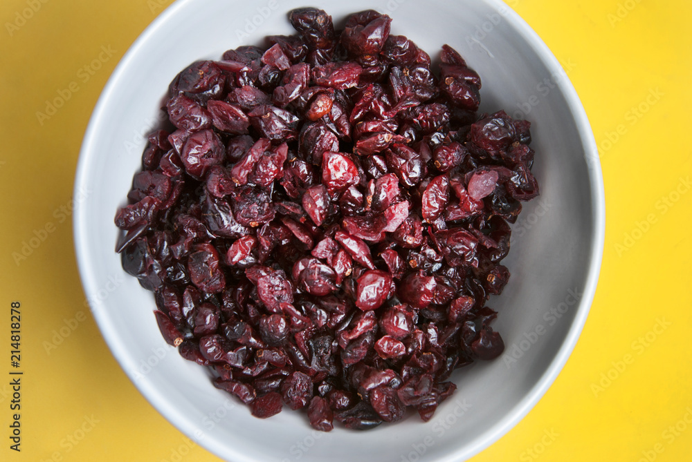 Dried fruits or berries, sweet cranberries isolated on yellow background in round white bowl. Ingredients for healthy breakfast. Top view. Dried fruits or berries, sweet cranberries isolated on yellow background in round white bowl. Ingredients for healthy breakfast. Top view.