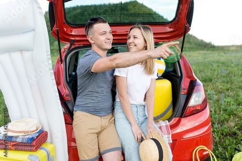 Beautiful young couple with collected travel suitcases and bags sitting in the trunk of a red car choosing the direction to travel
