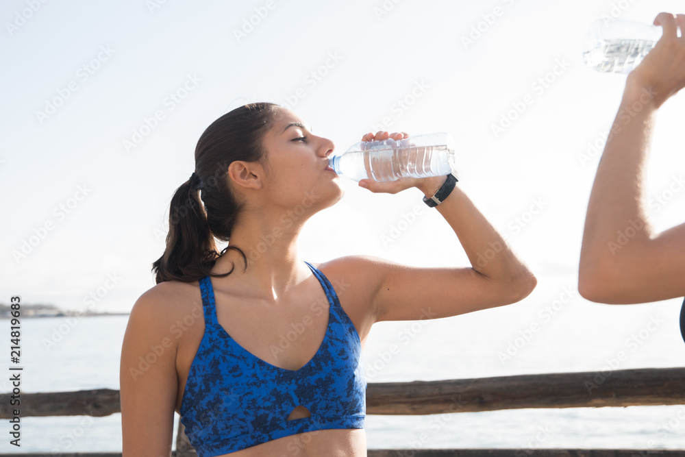 Two women drinking water from bottles near the sea Two women drinking water from bottles near the sea
