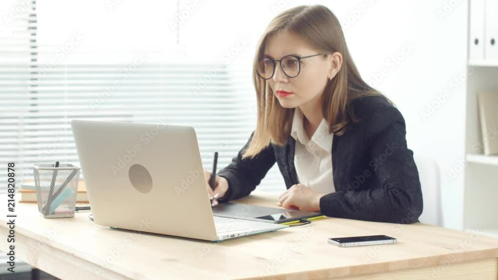 Young woman graphic designer working on laptop using tablet at modern office Young woman graphic designer working on laptop using tablet at modern office