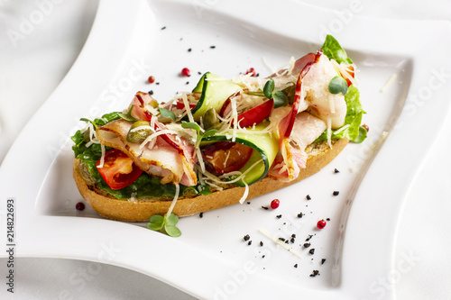 Bruschetta with bacon, fresh vegetables and capers on white plate