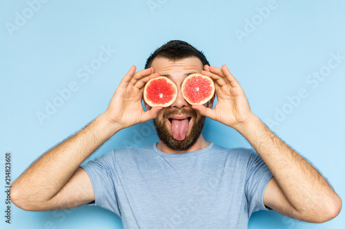 Young man holding slices of grapefruit in front of his eyes