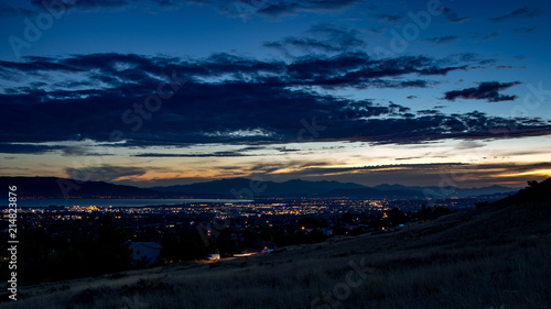 Dusk falls over a sleepy city in a valley with mountains and a lake in the background