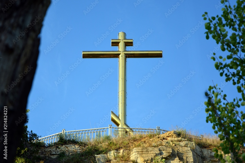 The Golden Cross on the top of the mountain shines in the sun against the blue sky. The Golden Cross on the top of the mountain shines in the sun against the blue sky.