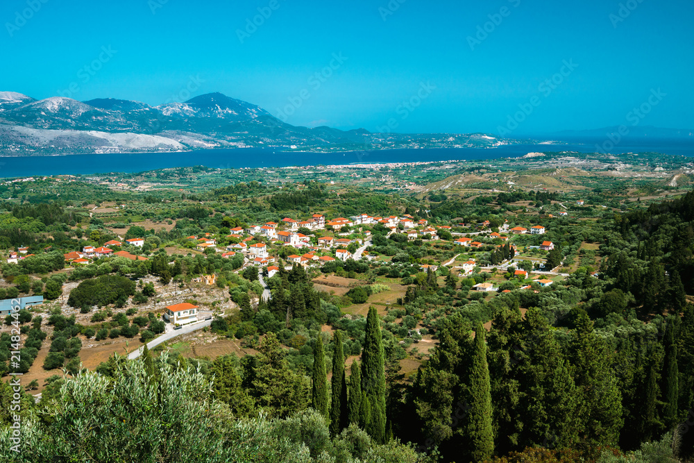 View of idyllic valley town with red roofs on mediterranean island. Olive groves, cypresses and blue bay in the distance