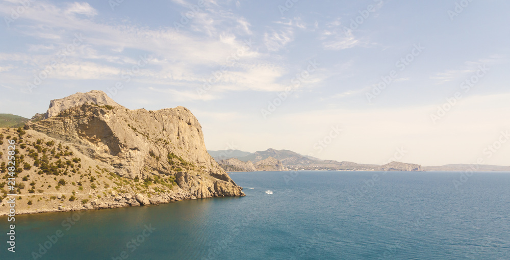 Calm blue sea off the coast of the New World (Novyi Svit) with beautiful clouds in the sky and mountains.Crimea.