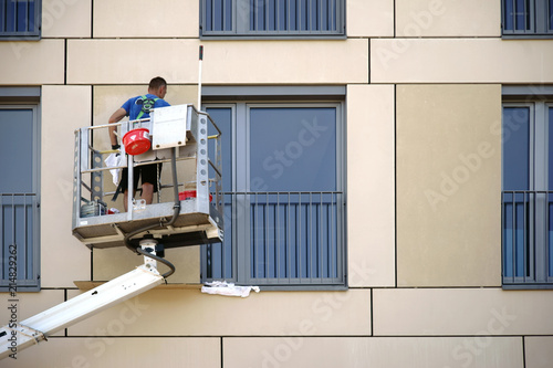 Fensterputzer putzt Fenster / Ein Fensterputzer steht auf einer Hebebühne und putzt die Fenster eines Hochhauses.