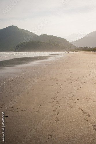 Ubatumirim  Ubatuba  Brazil - Empty and calm beach  with footsteps on the sand  mountains and clouds on background.