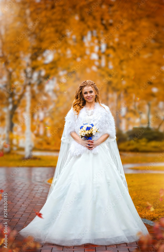 Charming bride holding bouquet of flowers, in an autumn park
