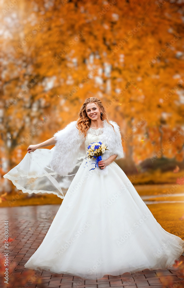 Happy bride in white dress and with bouquet of flowers walking in an autumn park