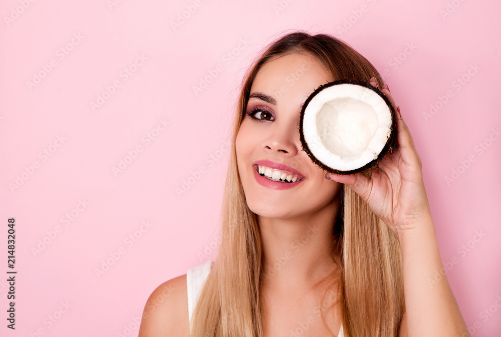Happy young woman holding coconut piece in front of eye Happy young woman holding coconut piece in front of eye