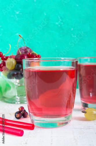 Berry compote. Fruit vitamin drink in glass and ripe fresh berries on a bright background. Vertical view