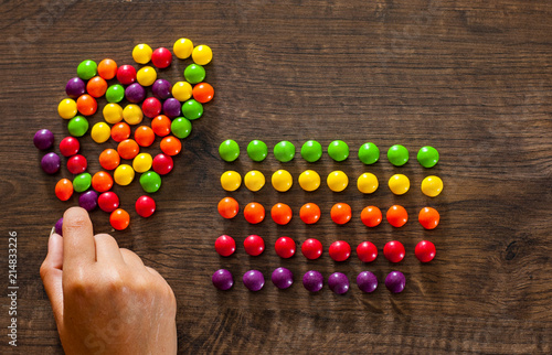 woman's hand collects even row of colorful candies on a wooden background