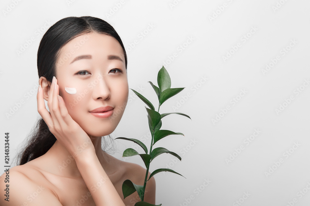 Close up of beauty portrait of beautiful Asian half naked woman applying face cream with plant, isolated on white background Close up of beauty portrait of beautiful Asian half naked woman applying face cream with plant, isolated on white background