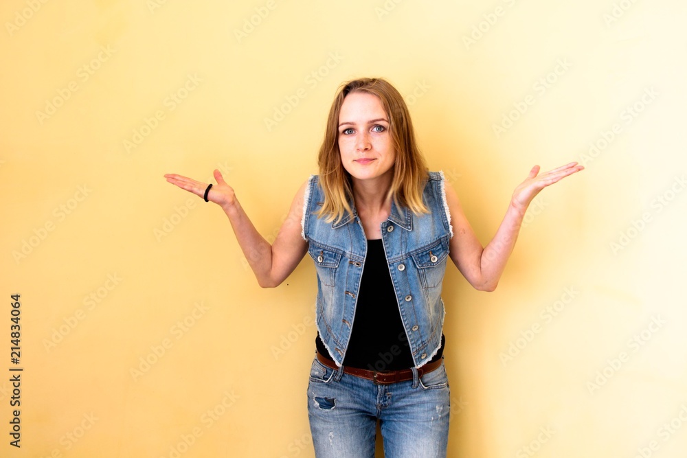 Beautiful girl with her hair standing on a yellow isolated background. She does not know what is happening and shows it with her whole appearance, shows it with her own hands and an expression on her Beautiful girl with her hair standing on a yellow isolated background. She does not know what is happening and shows it with her whole appearance, shows it with her own hands and an expression on her