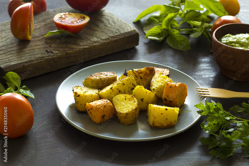 Baked potatoes, greenery sauce, fresh tomatoes, basil leaves and parsley on the kitchen table. Baked potatoes, greenery sauce, fresh tomatoes, basil leaves and parsley on the kitchen table.