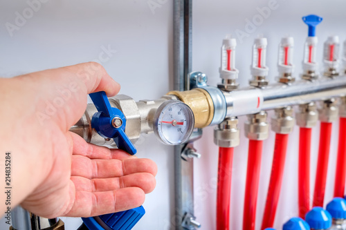 The men's hand opens the ball valve on supply pipeline on the collector for warm floor