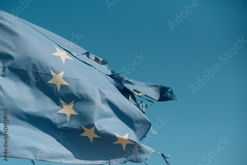 Torn EU flag wave on blue sky. European Union flag with twelve stars on sunny outdoor. Symbol of unity. Euro skepticism concept, copy space